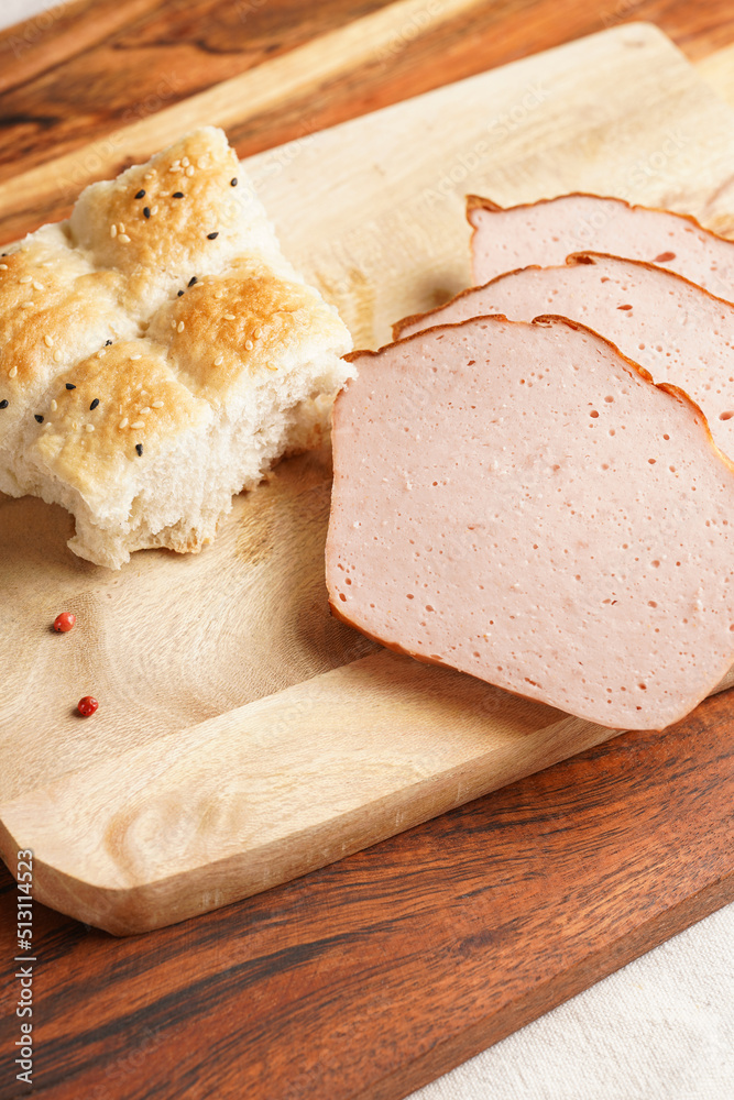 Traditional oven baked bavarian meal leberkäse sliced - meat dish made of corned beef, pork and bacon, finely ground and bakes as a bread loaf, on wooden board on dark wooden table with bread cubes