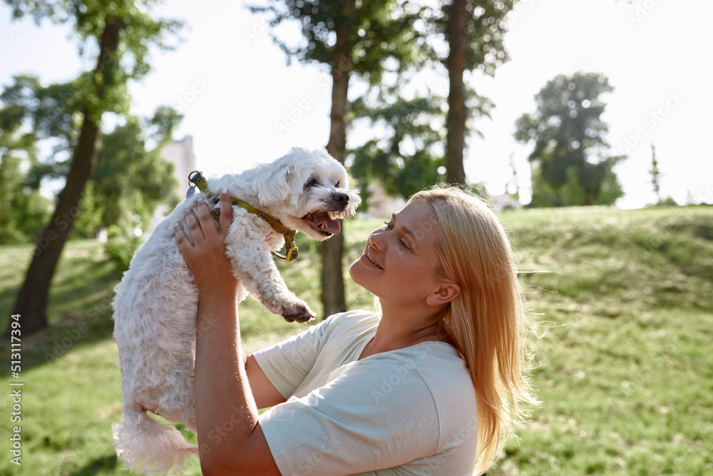 Girl hold and look at Maltese dog in blurred park Girl hold and look at Maltese dog in blurred park