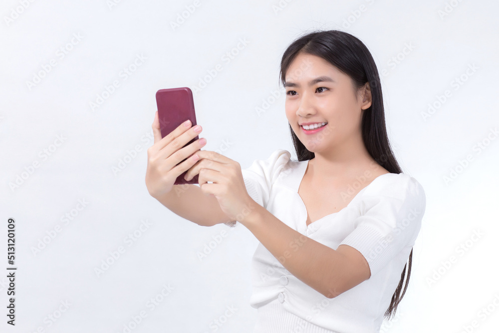 Portrait of Asian beautiful woman who has black long hair in white shirt, is holding the smartphone in her hand and smiling. She take a selfies photo on white background. Portrait of Asian beautiful woman who has black long hair in white shirt, is holding the smartphone in her hand and smiling. She take a selfies photo on white background.