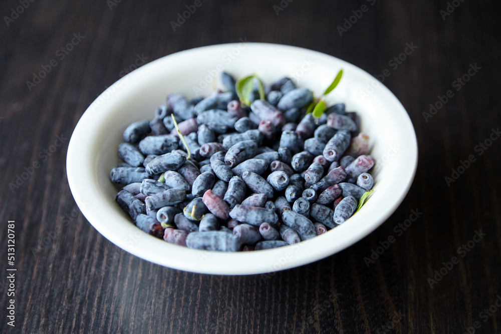 Haskap berry with fresh green leaves in white bowl on wooden table. Honeyberry (Lonicera caerulea) Haskap berry with fresh green leaves in white bowl on wooden table. Honeyberry (Lonicera caerulea)