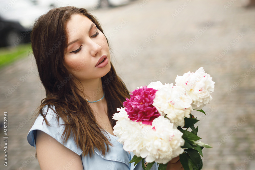 A beautiful young woman in a blue dress with a bouquet of peonies.