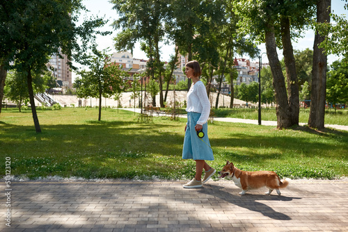 Side view of girl walking cute Corgi dog in park
