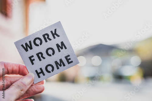 work from home sign being hold in front of out of focus backyard and home exterior, digital nomads working remotely or wfh days during lockdowns