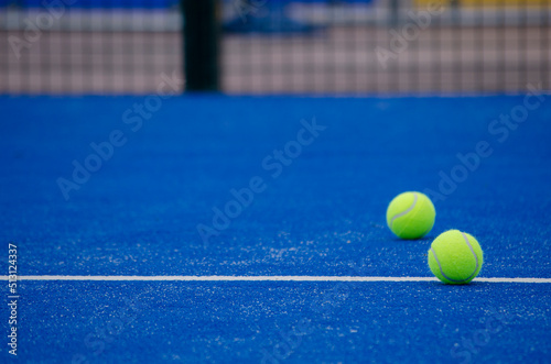 two paddle tennis balls over the line of a blue paddle tennis court © Vic