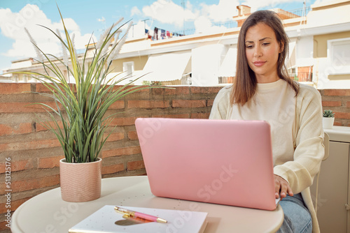 young woman working on the terrace of her house with her laptop and smartphone