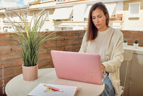 young woman working on the terrace of her house with her laptop and smartphone