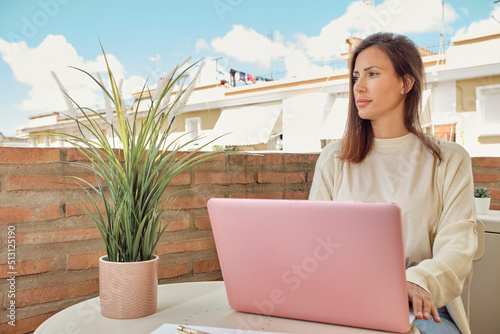 young woman working on the terrace of her house with her laptop and smartphone