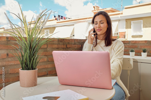 young woman working on the terrace of her house with her laptop and smartphone