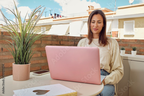 young woman working on the terrace of her house with her laptop and smartphone