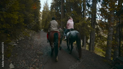 camera follows women tourists riders on horseback walks by trail in woods in Carpathian mountains in Ukraine. Excursions and sightseeing at vacation. travel, exploring wild life, nature hiking photo