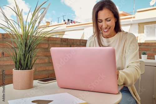 young woman working on the terrace of her house with her laptop and smartphone