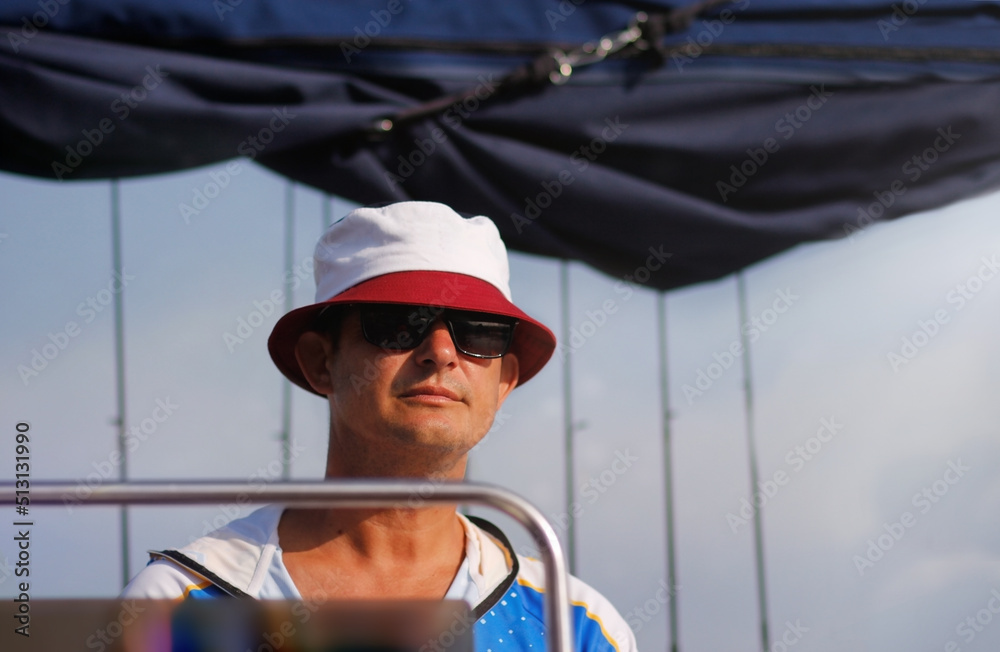 a brutal 45-year-old man in sunglasses and a panama hat stands at the helm of a high-speed boat riding on the sea. a brutal 45-year-old man in sunglasses and a panama hat stands at the helm of a high-speed boat riding on the sea.