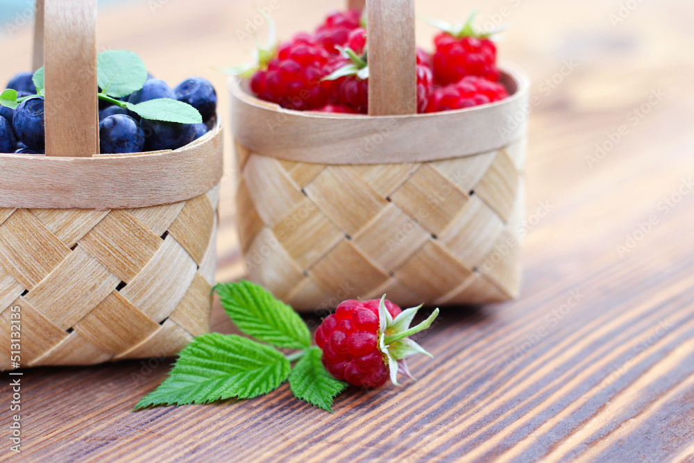 blueberries and raspberries in small baskets made of birch bark on a wooden background. harvest of wild berries, vitamins and health benefits.