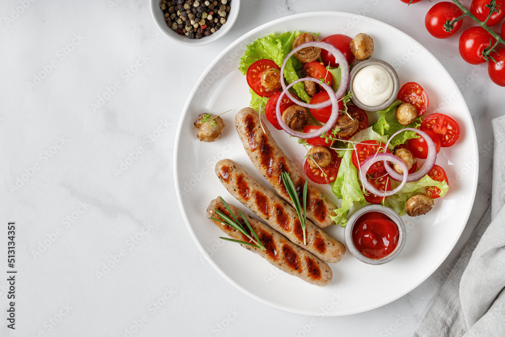 Dish with Grilled sausages and vegetable salad with lettuce and tomatoes on white plate and marble background. Top view, copy space. BBQ