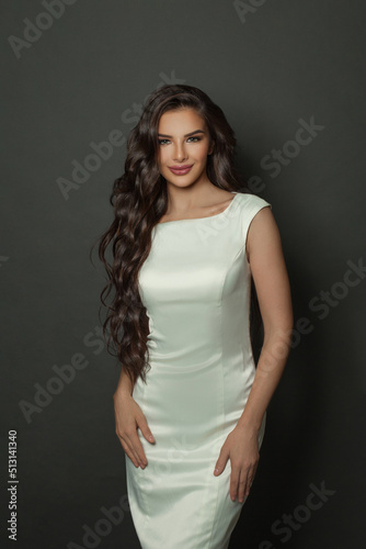 Perfect brunette woman with long wavy hairstyle in white silky dress posing on black studio background © millaf