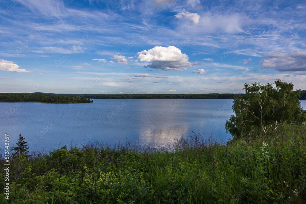 A picturesque summer landscape with views of the lake, forest and sky with clouds.