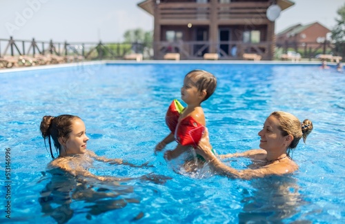 Mom plays with her daughter and little son in oversleeves in the pool on summer vacation photo