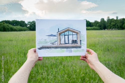 Architect holding barn house  hand drawn sketch in front of a plot of land photo