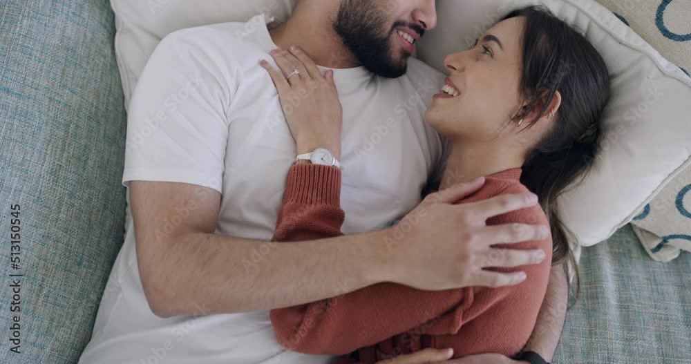 Above loving couple lying in bed kissing each other good morning. Happy husband and wife cuddling in bed together in their modern bedroom. Young married couple waking up together in their new home