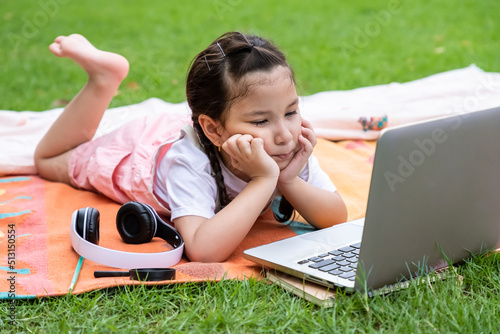 Happy Caucasian girl child smiling, looking and using at laptop computer in park. Learning online education concept.