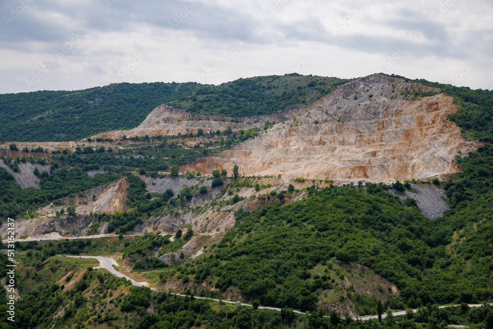 Natural quarry is located near road against backdrop of Rhodope Mountains and hills with forests and mountain vegetation