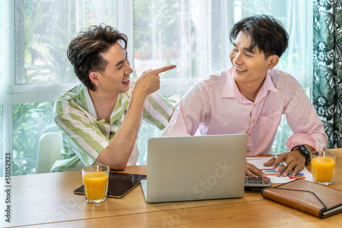 Cute Asian LGBT gay man couple, using laptop working at home, spend time together. Healthy lifestyle with orange juice.