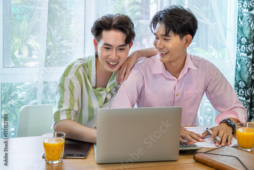 Cute Asian LGBT gay man couple, using laptop working at home, spend time together. Healthy lifestyle with orange juice.