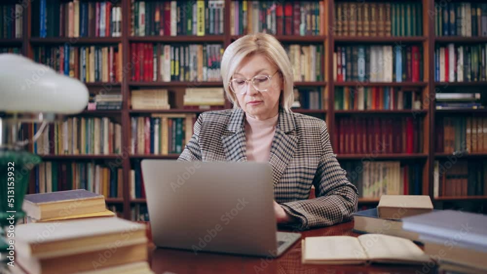 Serious woman in her 50s working with laptop in library, scientific research Serious woman in her 50s working with laptop in library, scientific research