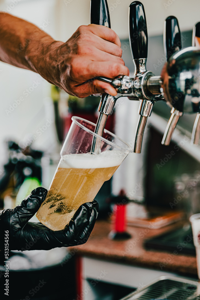 hand at beer tap pouring a draught beer in plastic glass serving in a cafe