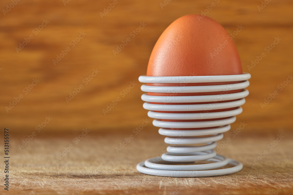 One boiled egg in a spiral-shaped white metal support on wood One boiled egg in a spiral-shaped white metal support on wood