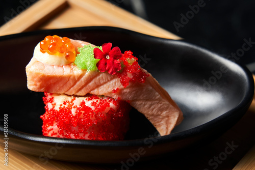 Piece of sushi ingredients: salmon, caviar, Masago, Ikura, Tobico on a black plate. Front view. Close-up Food concept photo