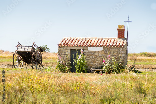 Petite maison en pierres avec girouette et une charrette en bois. Marais des Ileaux, Noirmoutier photo