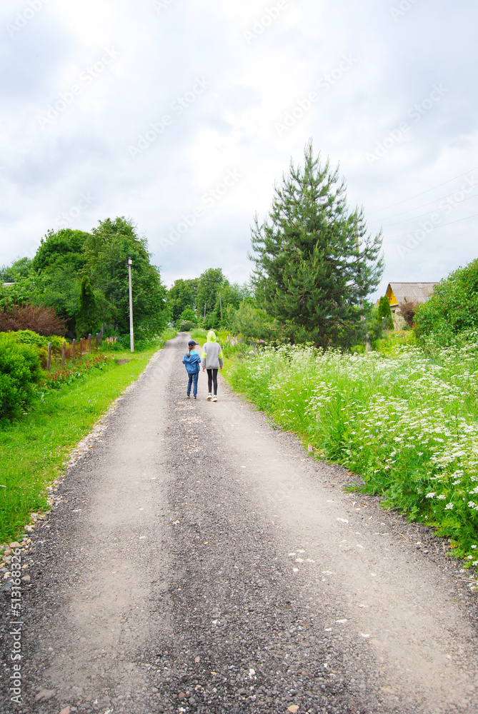 Children walk along the road in the village. Summer village landscape. Walking along a rural road. The road in the village.