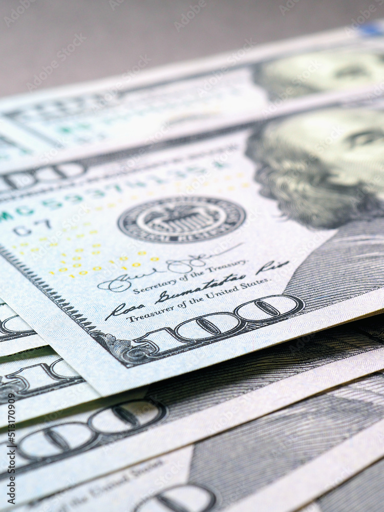 American paper money. Several one hundred dollar notes lie on a gray textured surface. Focus on the number 100. Vertical illustration about savings economy and US dollar. National debt and Treasury