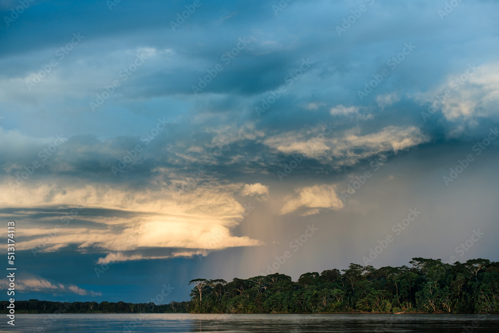 a distant rain falls on the Amazon rainforest with a river in the foreground
