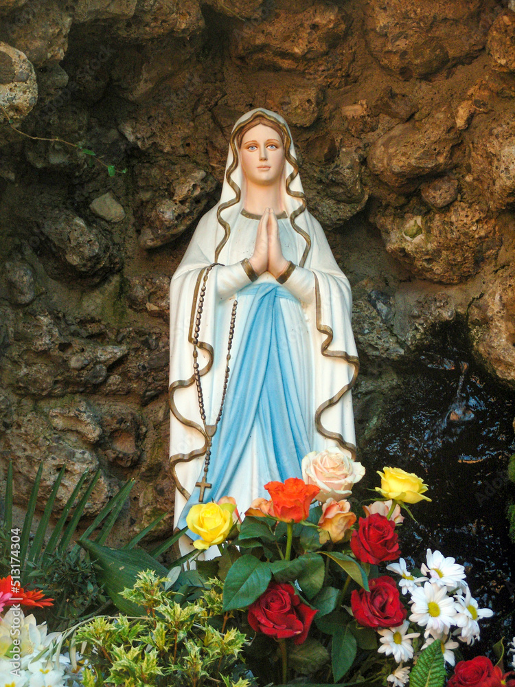 statue of the virgin mary in a small cave with flowers of different colors
