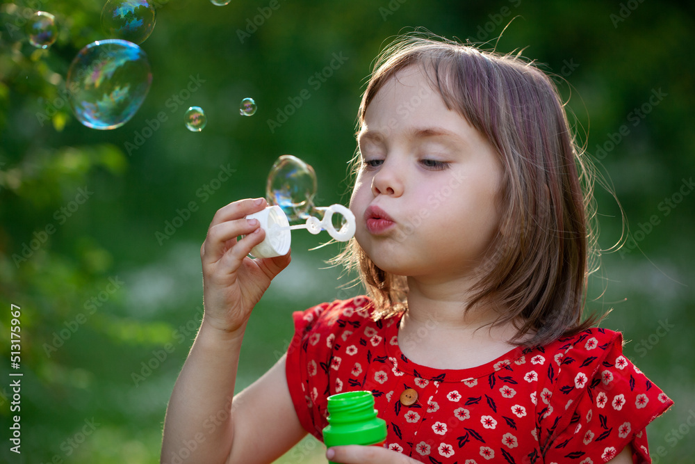 Little child girl in red dress blowing soap bubbles on a summer day at green nature background. Little child girl in red dress blowing soap bubbles on a summer day at green nature background.
