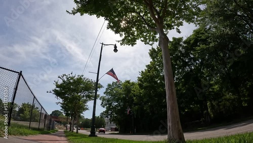 footage of an American flag on a tall curves lamp post flying in the wind surrounded by lush green trees with cars driving down the street in Douglasville Georgia USA photo