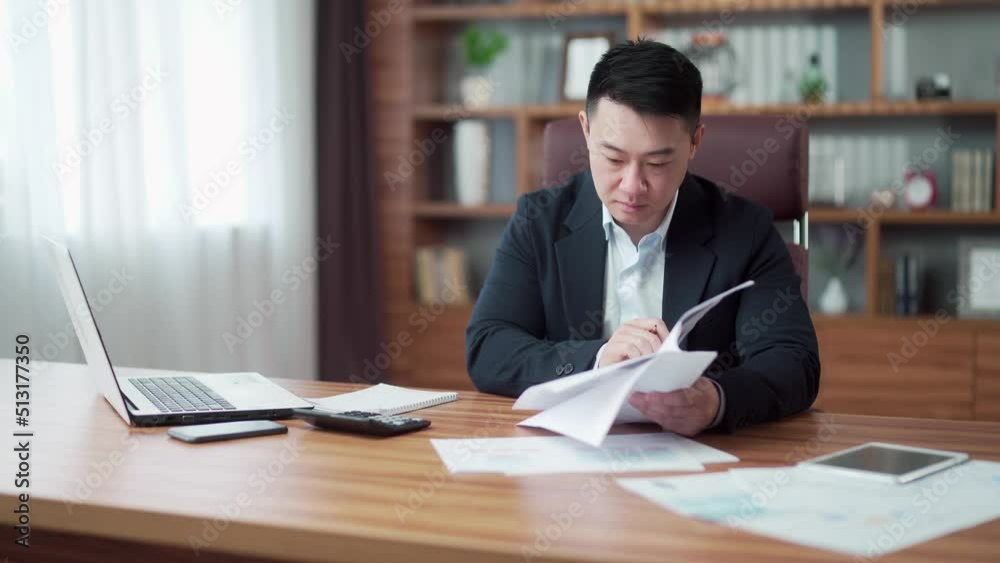 focused asian business man signs a contract reviews financial documents or report. Businessman working with documentation at workplace in office. Employee entrepreneur in a suit is busy counting bills