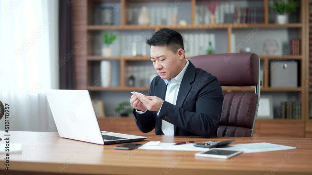 Mature businessman Asian male worker suffers from headache allergies, sneezes with a runny nose. Employee coughs a cold or flu sitting at work in the office. Indoor. Feeling unwell in a business man