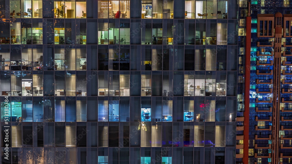 Night aerial view of office or apartment building glass window facade with illuminated lighted workspace rooms timelapse.