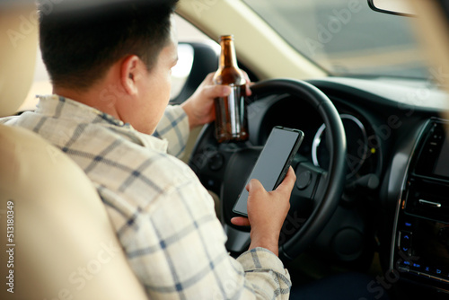 Drunk man holding bottle of beer and using smartphone while driving a car, campaigning for drunken not driving avoiding accidents on road, Don't drink and drive concept.
