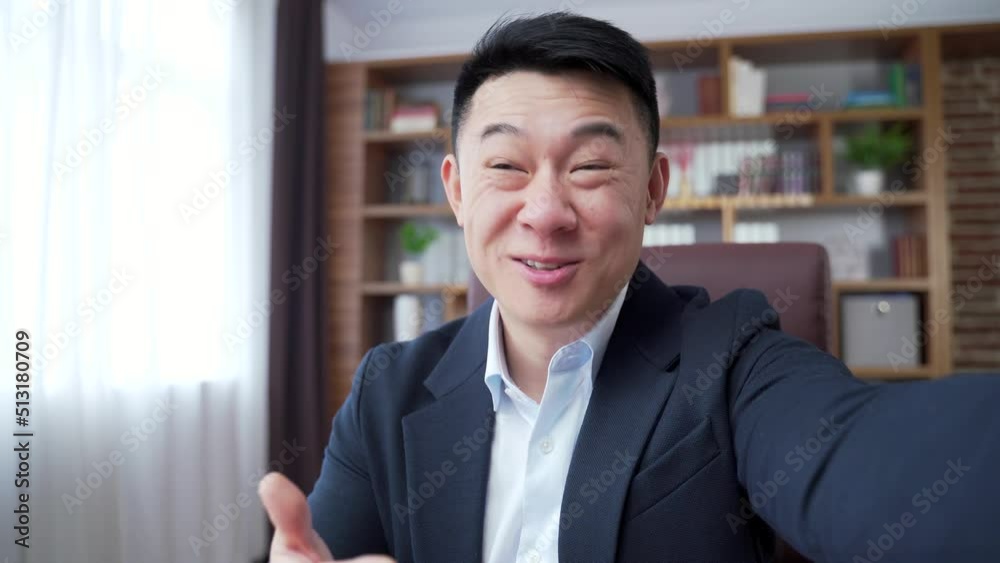happy asian businessman talking on call on smartphone front camera in office. Business man worker communicating online view of mobile phone webcam. looks at camera waves cheerful employee laugh asia happy asian businessman talking on call on smartphone front camera in office. Business man worker communicating online view of mobile phone webcam. looks at camera waves cheerful employee laugh asia