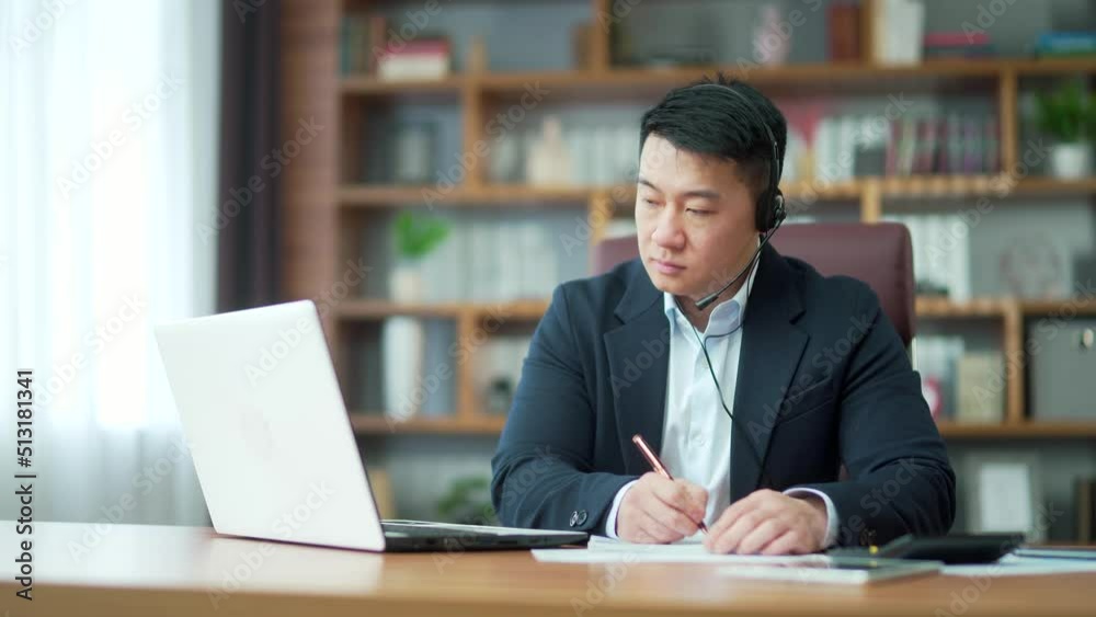 Asian employee studying online virtual tutor using laptop in office. distant worker wears headphones video calling makes notes, elearning with teacher, attending remote conference meeting training