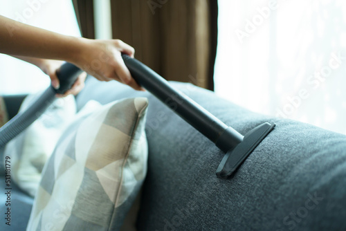 Asian housewife using a wireless vacuum machine to clean a sofa in living room.