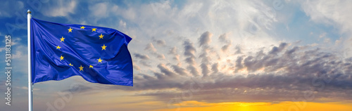 Flag of the European Union waving in the wind on flagpole against background of the sunrise, banner, close-up