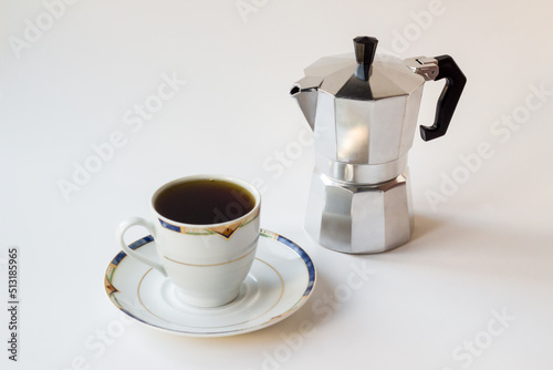 Tradtitional Italian Metal Coffee Maker on white surface with a cup of coffee