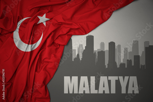 abstract silhouette of the city with text Malatya near waving national flag of turkey on a gray background. photo