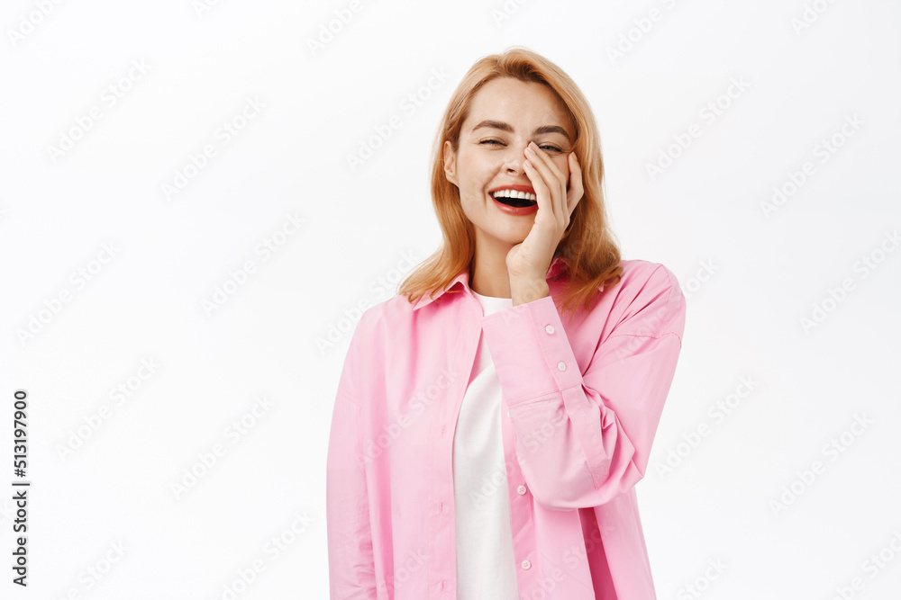 Genuine young woman laughing, touching face and smiling sincere, standing over white background Genuine young woman laughing, touching face and smiling sincere, standing over white background