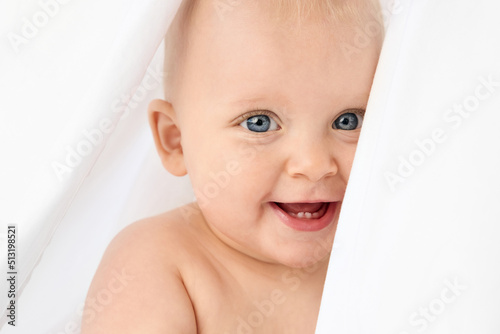 Close-up portrait of blue-eyed baby peeking behind white sheet